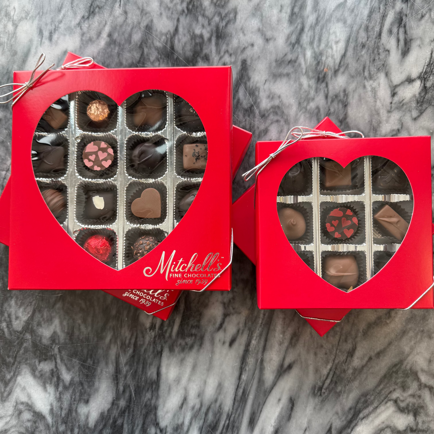 Two red heart-shaped chocolate boxes with Mitchell's branding on a marble background