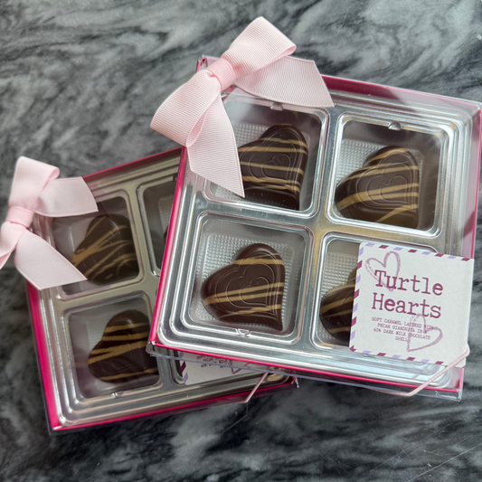 Two boxes of chocolate turtle hearts with pecans and caramel, with pink bows on a marble surface sold by Mitchell's Chocolates in Cleveland