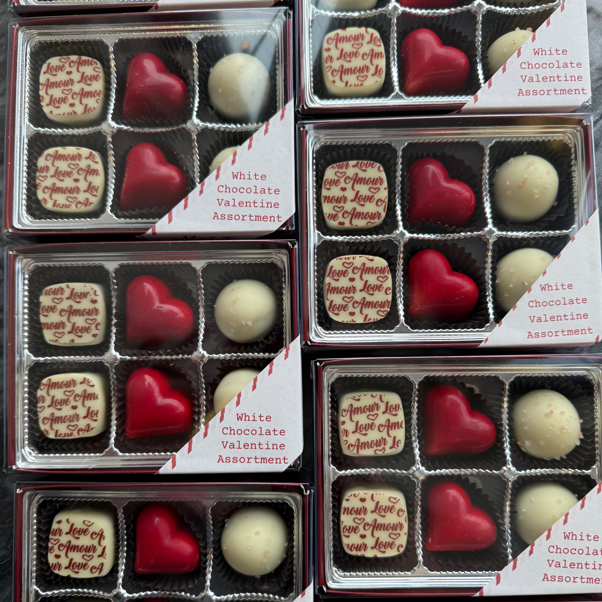 Assorted white chocolate Valentine's Day truffles in clear packaging with red and white labels.
