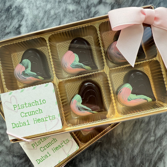 Box of Pistachio Crunch Dubai Hearts chocolates with a pink ribbon on a marble surface